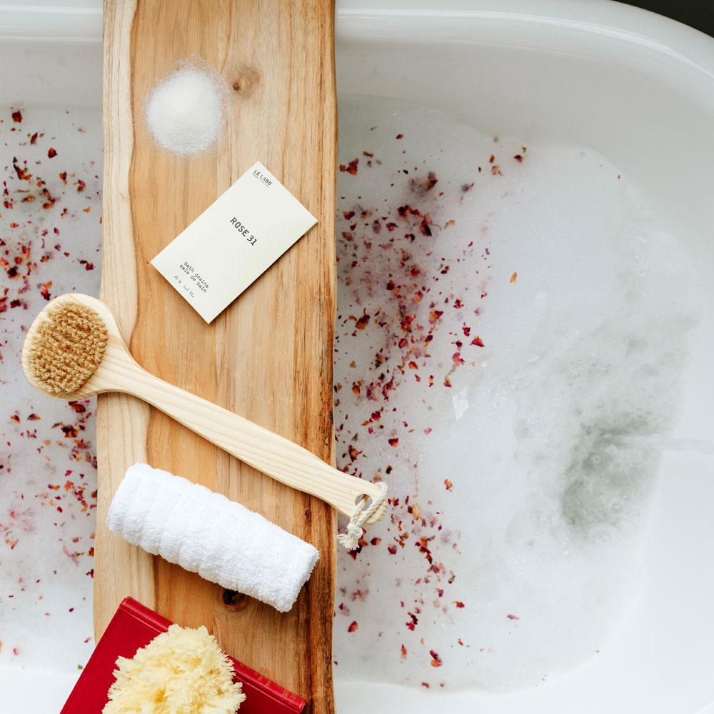 Le Labo Rose 31 Bath Salts on tray in bath tub with rose petals